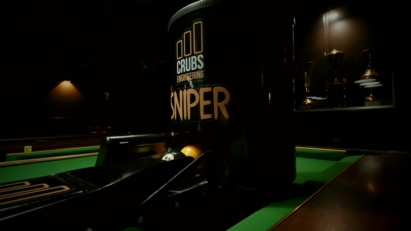 Le Sniper installé dans un club, vitrine à trophées en arrière-plan.