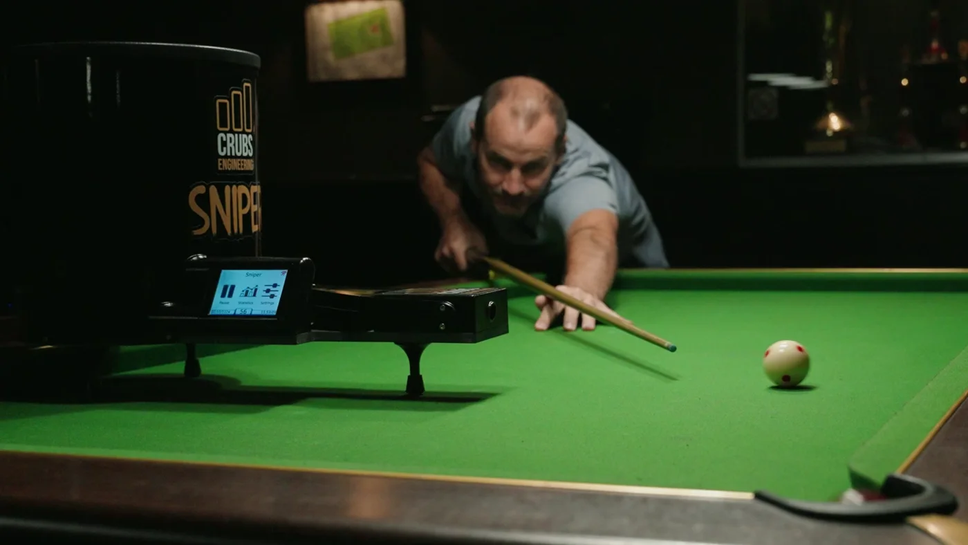 Le Sniper installé sur une table de billard, un joueur vise une bille blanche.